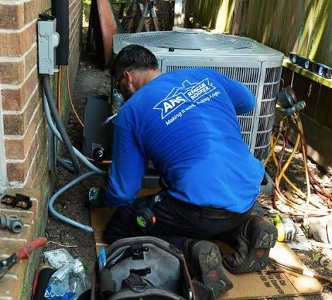 Technician repairing connections beside a residential air conditioner
